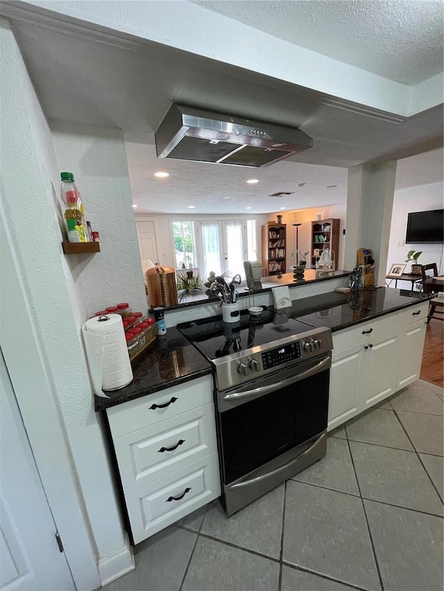 kitchen featuring stainless steel range with electric stovetop, range hood, light tile patterned flooring, a textured ceiling, and white cabinets