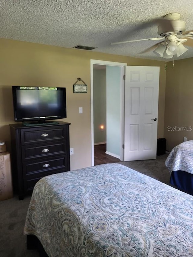 bedroom featuring a ceiling fan, visible vents, dark carpet, and a textured ceiling