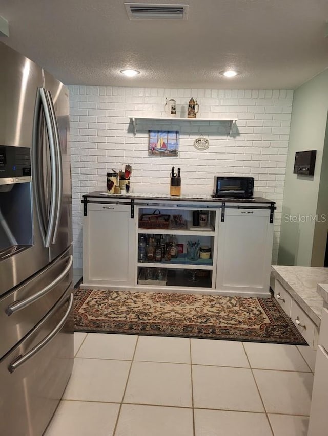 kitchen featuring white cabinets, stainless steel fridge with ice dispenser, a textured ceiling, and light tile patterned floors