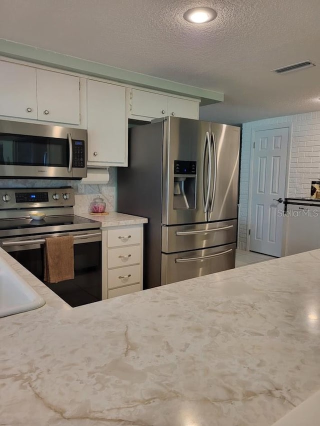 kitchen with light stone countertops, a textured ceiling, stainless steel appliances, and backsplash