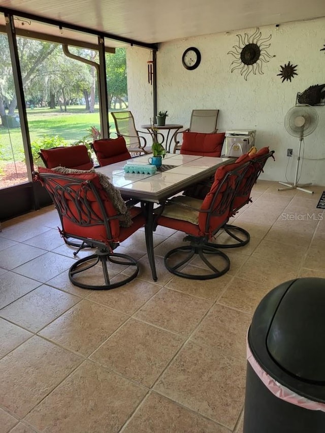 dining space featuring light tile patterned floors, a sunroom, and a textured wall