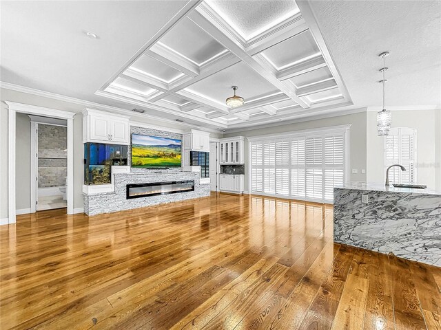 unfurnished living room with sink, coffered ceiling, wood-type flooring, ornamental molding, and beamed ceiling