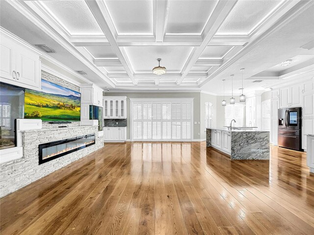 unfurnished living room featuring crown molding, beam ceiling, coffered ceiling, a fireplace, and light wood-type flooring