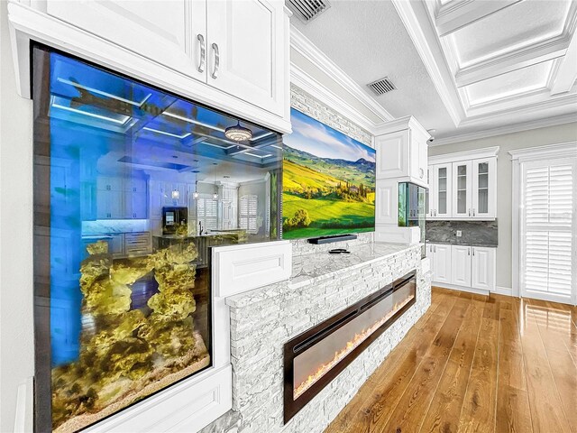 kitchen with white cabinetry, light stone counters, wood-type flooring, ornamental molding, and backsplash