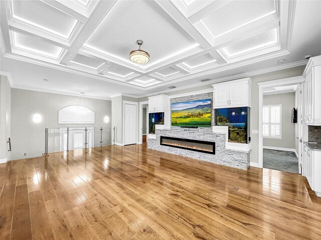 living room featuring a stone fireplace, beamed ceiling, ornamental molding, coffered ceiling, and light wood-type flooring