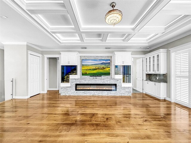 unfurnished living room featuring coffered ceiling, a stone fireplace, ornamental molding, and light hardwood / wood-style floors