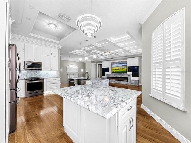 kitchen with appliances with stainless steel finishes, a kitchen island with sink, white cabinetry, hanging light fixtures, and light stone counters