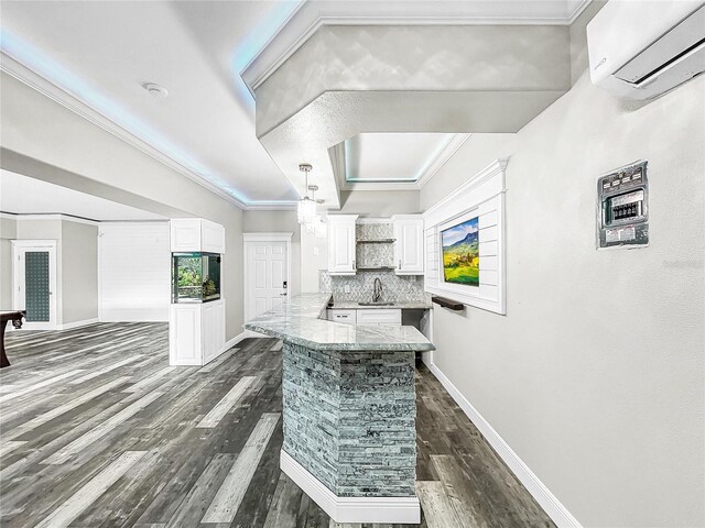 kitchen with crown molding, dark hardwood / wood-style floors, a wall unit AC, and white cabinets