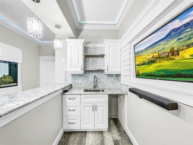 kitchen featuring white cabinetry, sink, hanging light fixtures, light stone counters, and crown molding