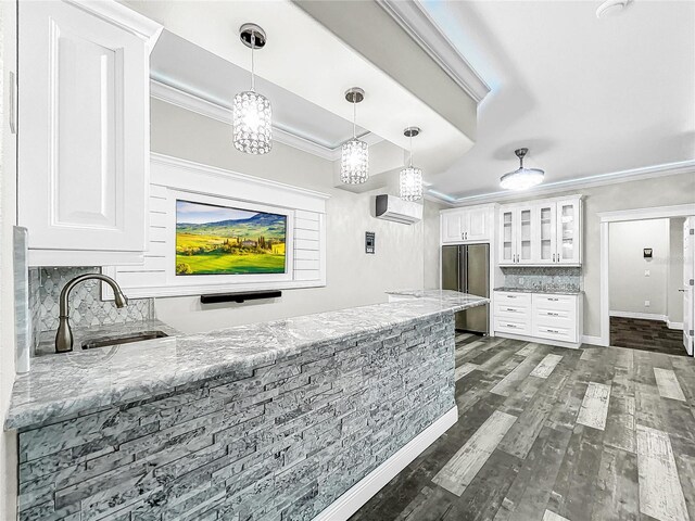 kitchen featuring light stone counters, a wall mounted air conditioner, high quality fridge, ornamental molding, and white cabinets