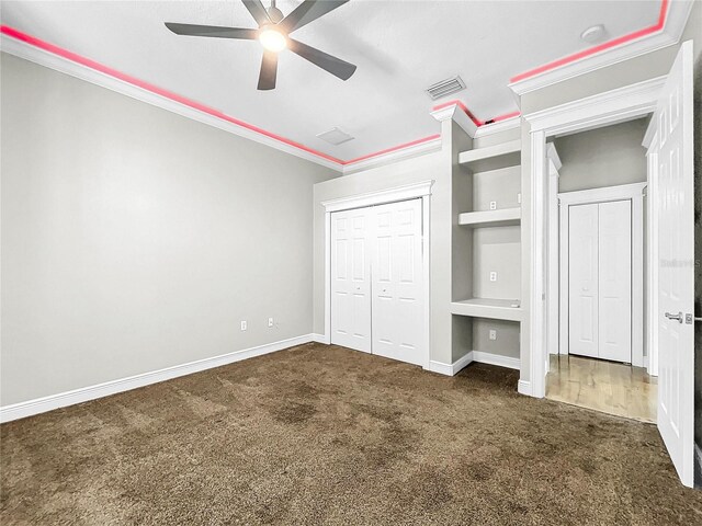 unfurnished bedroom with dark colored carpet, ceiling fan, crown molding, and a closet