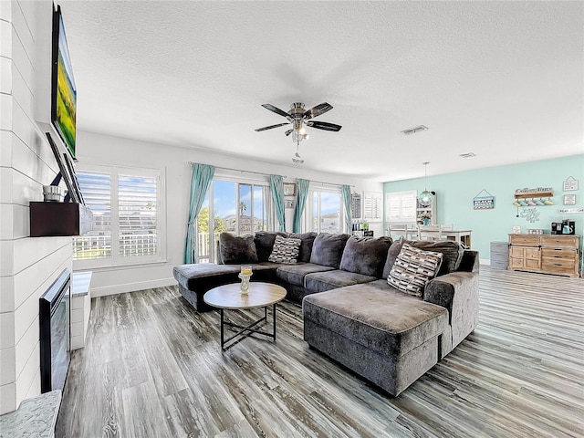 living room featuring hardwood / wood-style floors, a fireplace, a textured ceiling, and ceiling fan