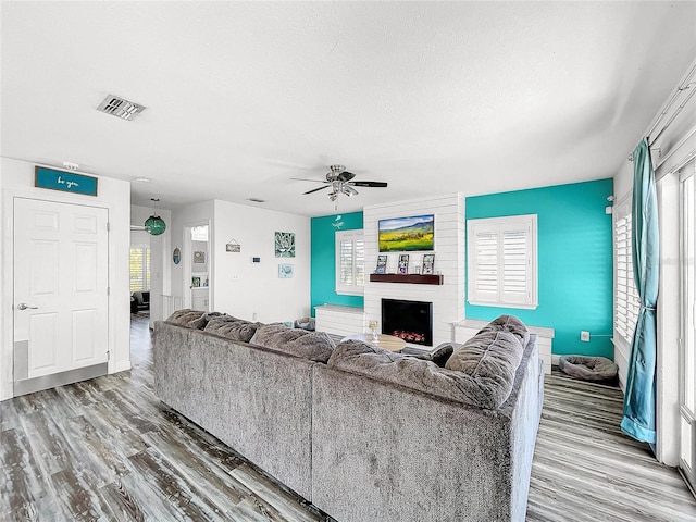 living room with wood-type flooring, ceiling fan, a textured ceiling, and a fireplace