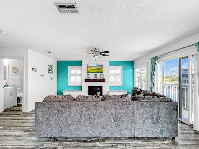 living room with wood-type flooring, a textured ceiling, ceiling fan, and a fireplace