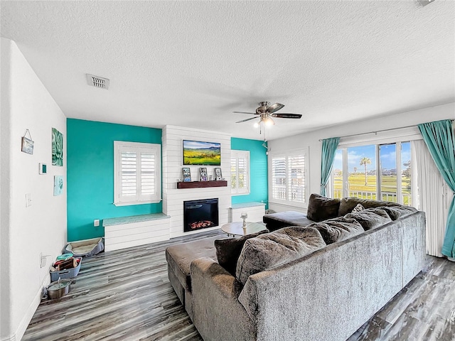 living room with ceiling fan, wood-type flooring, a fireplace, and a textured ceiling