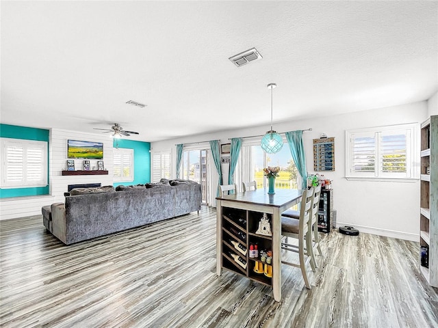 dining area featuring wood-type flooring, a large fireplace, ceiling fan, and a textured ceiling