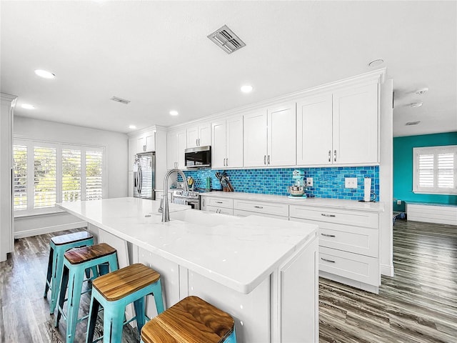 kitchen featuring stainless steel appliances, a kitchen island with sink, a breakfast bar area, and white cabinets