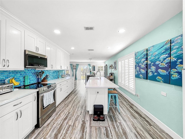 kitchen with white cabinetry, appliances with stainless steel finishes, an island with sink, and decorative backsplash