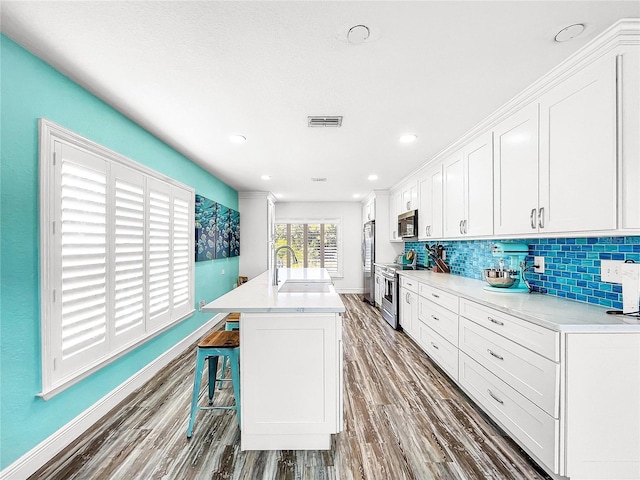 kitchen with sink, white cabinets, decorative backsplash, stainless steel appliances, and a center island with sink