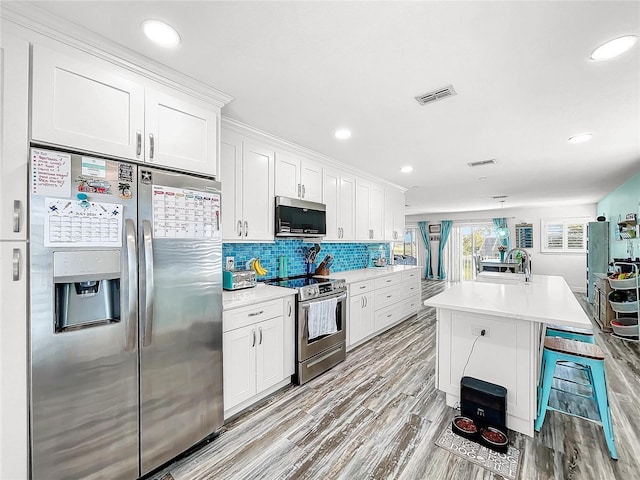 kitchen featuring light hardwood / wood-style flooring, appliances with stainless steel finishes, an island with sink, decorative backsplash, and white cabinets