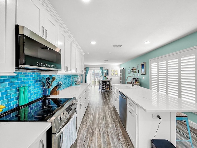 kitchen with appliances with stainless steel finishes, white cabinetry, sink, hardwood / wood-style flooring, and light stone countertops