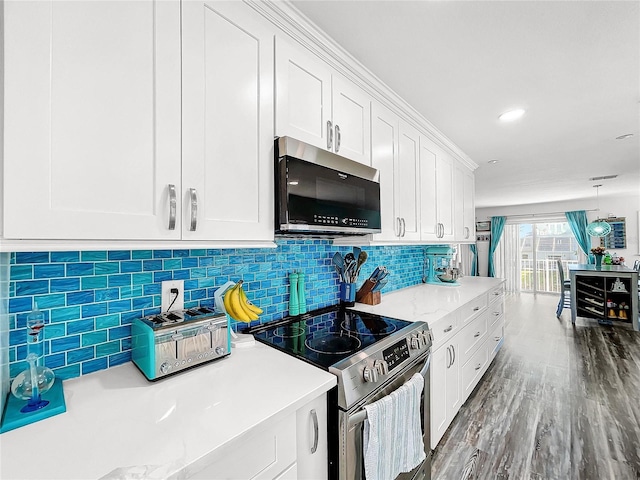 kitchen with appliances with stainless steel finishes, hardwood / wood-style floors, decorative light fixtures, white cabinetry, and backsplash