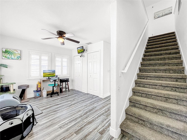 stairs with hardwood / wood-style floors and ceiling fan