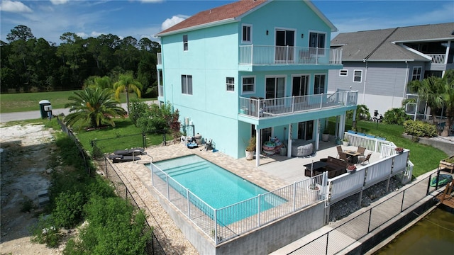 back of property featuring a fenced in pool, a patio, a balcony, and a lawn