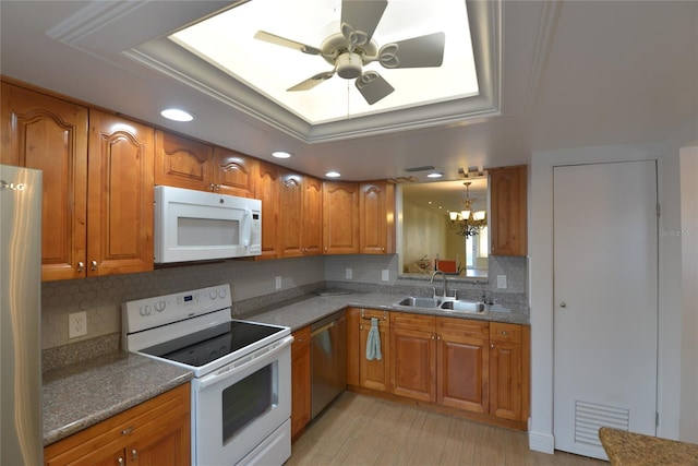 kitchen with white appliances, ceiling fan with notable chandelier, a tray ceiling, decorative light fixtures, and sink