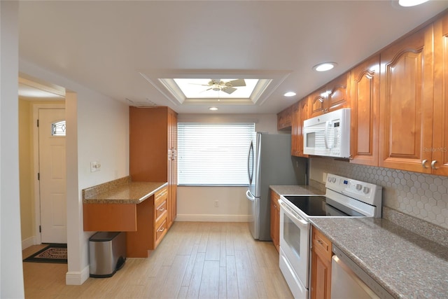 kitchen with tasteful backsplash, ceiling fan, white appliances, a skylight, and light hardwood / wood-style floors