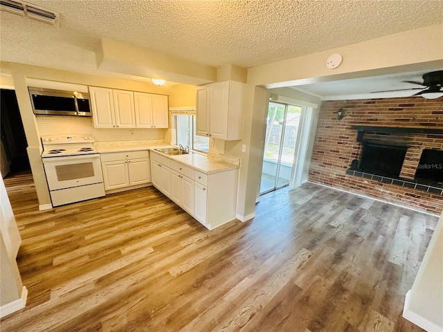 kitchen with white cabinetry, electric stove, ceiling fan, light hardwood / wood-style floors, and a brick fireplace