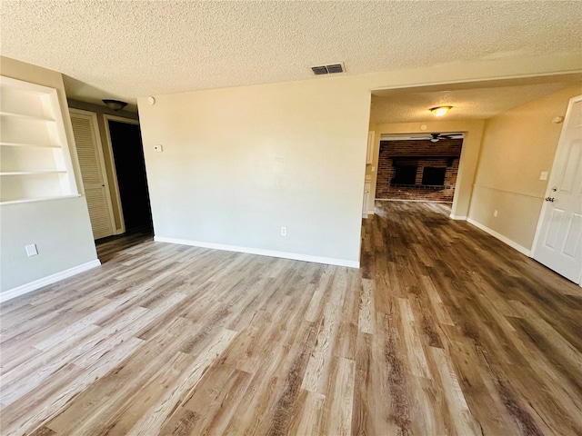 unfurnished living room with built in shelves, wood-type flooring, a brick fireplace, and a textured ceiling