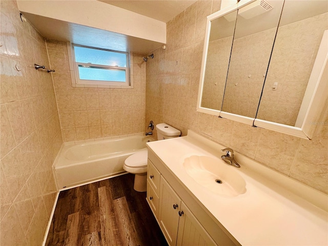 full bathroom with tile walls, tiled shower / bath, toilet, vanity, and hardwood / wood-style flooring