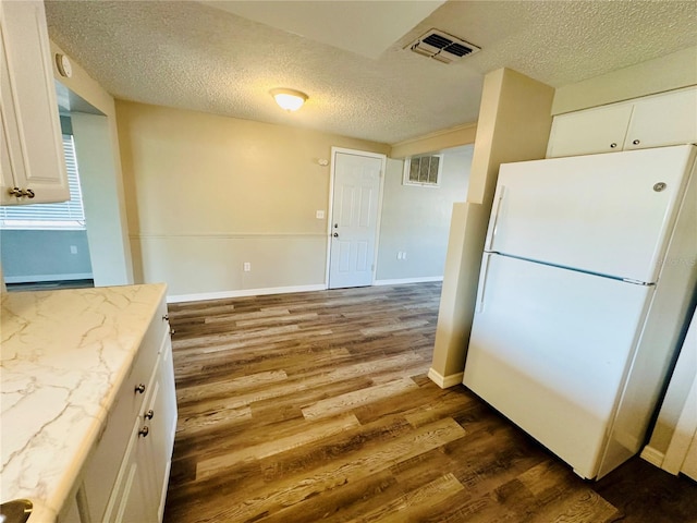 kitchen with white refrigerator, light stone counters, a textured ceiling, white cabinetry, and hardwood / wood-style flooring