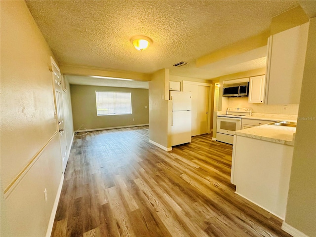 kitchen with light hardwood / wood-style flooring, a textured ceiling, white cabinets, and white appliances