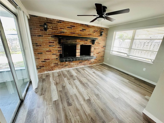 unfurnished living room featuring wood-type flooring, a brick fireplace, brick wall, and ceiling fan