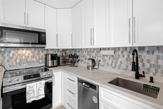 kitchen with white cabinets, sink, light stone counters, appliances with stainless steel finishes, and backsplash