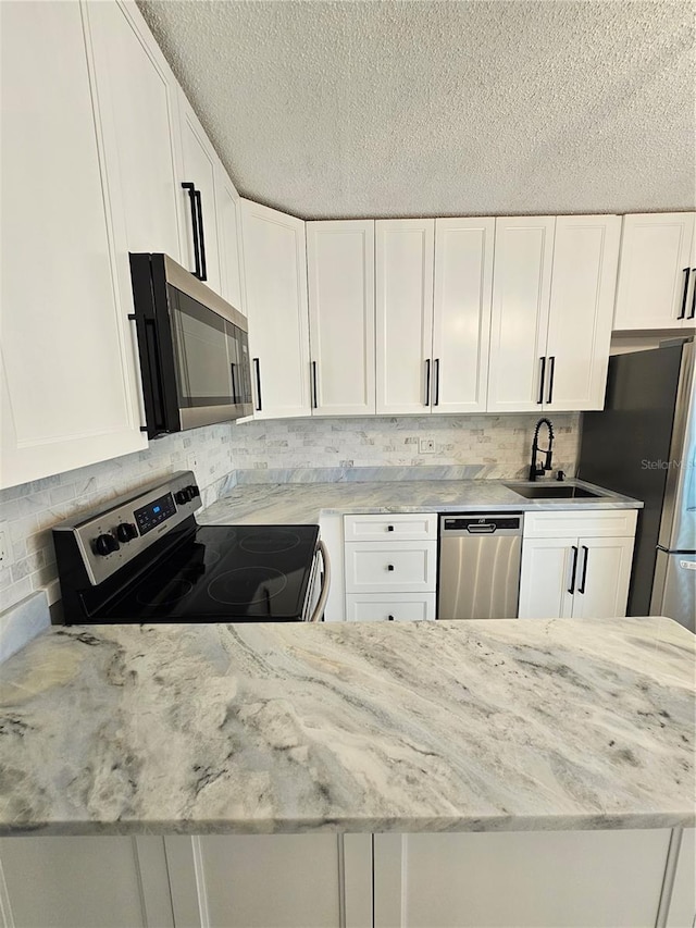 kitchen with appliances with stainless steel finishes, tasteful backsplash, white cabinets, sink, and light stone counters