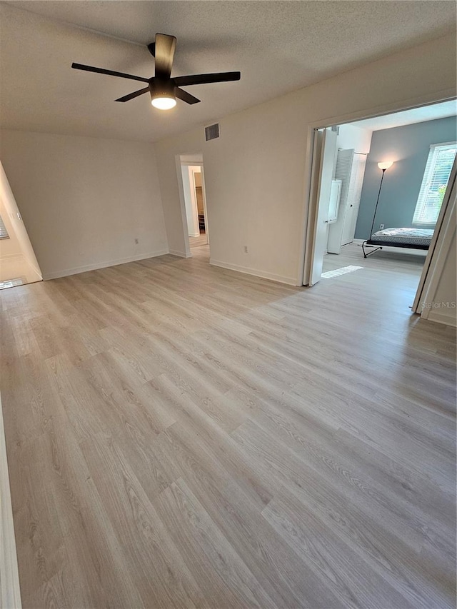 empty room with a textured ceiling, light wood-type flooring, and ceiling fan