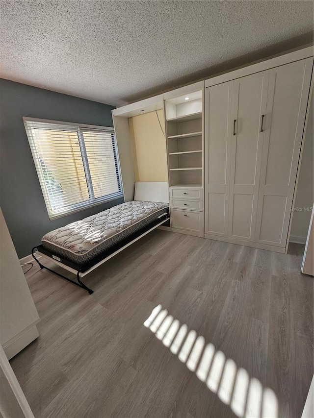 unfurnished bedroom with hardwood / wood-style flooring, a spacious closet, a closet, and a textured ceiling