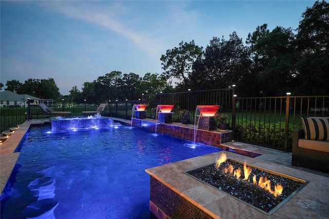 pool at dusk with a patio, pool water feature, and an outdoor fire pit