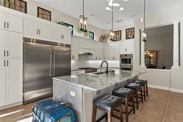 kitchen with appliances with stainless steel finishes, decorative backsplash, pendant lighting, and ornate columns