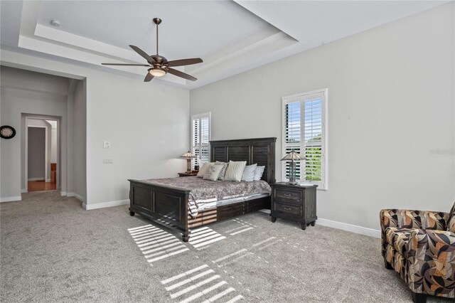 carpeted bedroom featuring ceiling fan and a tray ceiling