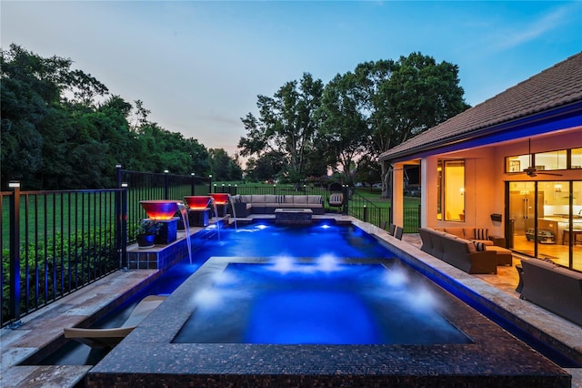 pool at dusk featuring an outdoor living space, pool water feature, an in ground hot tub, a lawn, and a patio