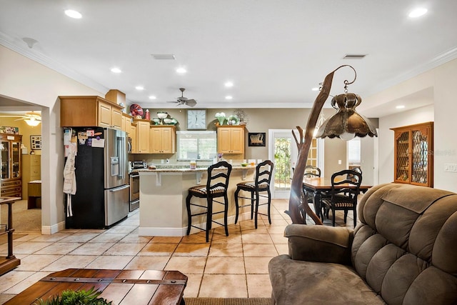 kitchen featuring crown molding, a kitchen breakfast bar, stainless steel appliances, light brown cabinets, and light tile patterned flooring