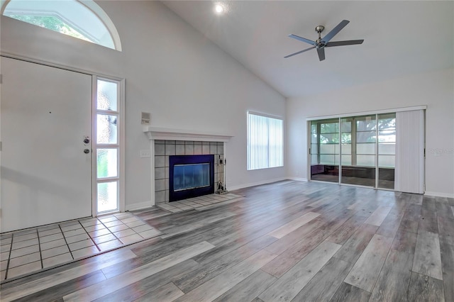 unfurnished living room with high vaulted ceiling, a fireplace, ceiling fan, and light wood-type flooring