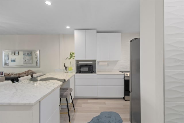 kitchen featuring black microwave, light stone countertops, light wood-type flooring, a peninsula, and white cabinetry