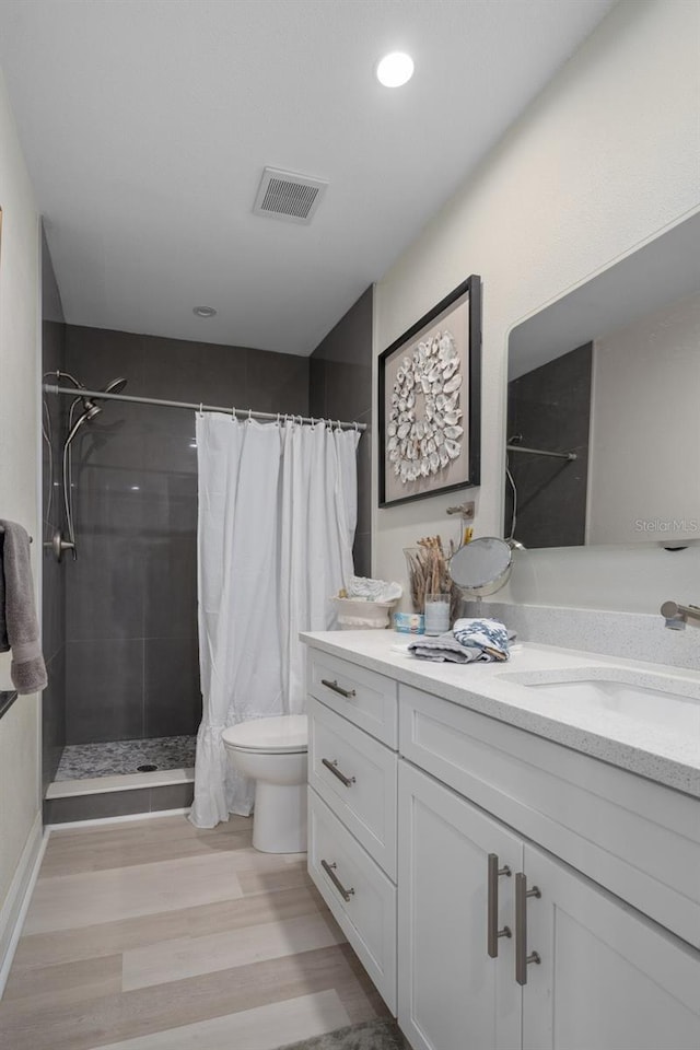 bathroom featuring vanity, wood finished floors, visible vents, a tile shower, and toilet