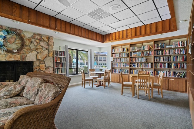 living area featuring a drop ceiling, built in features, wall of books, carpet flooring, and a fireplace