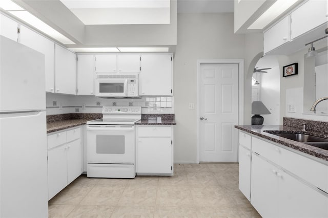 kitchen featuring dark stone counters, white appliances, white cabinets, sink, and light tile patterned floors